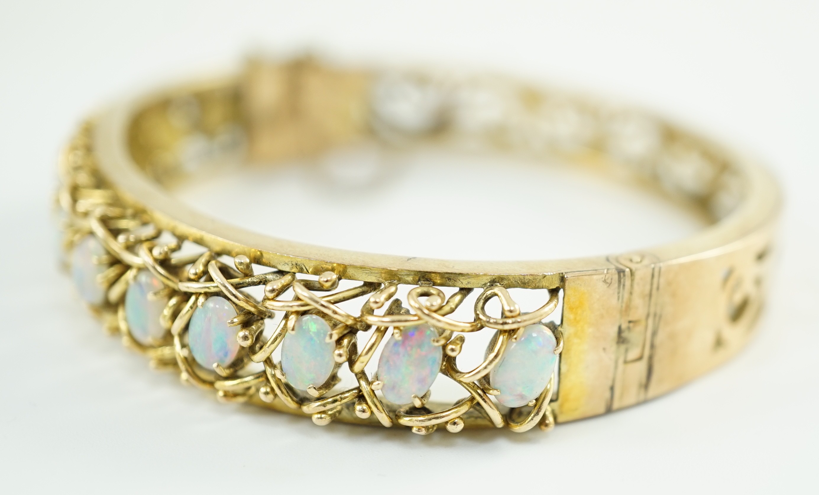 A pierced gold and twelve stone oval white opal set hinged bangle